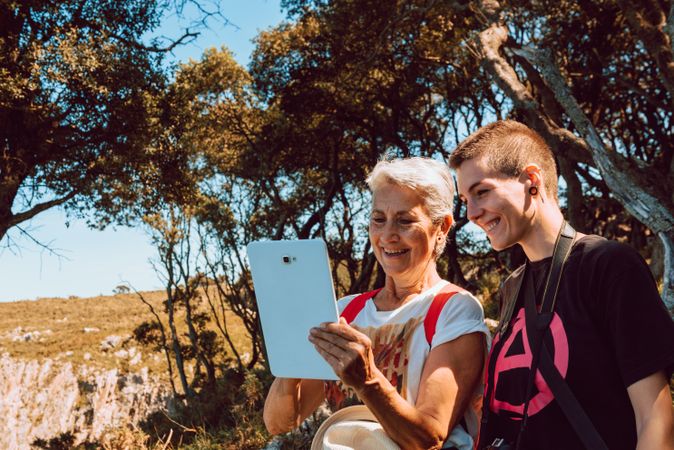 Older woman with young person looking at tablet sitting on stone in valley