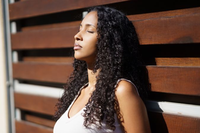 A Serene Woman Joyfully Enjoying the Warm Sunshine While Leaning Against a Rustic Wooden Wall