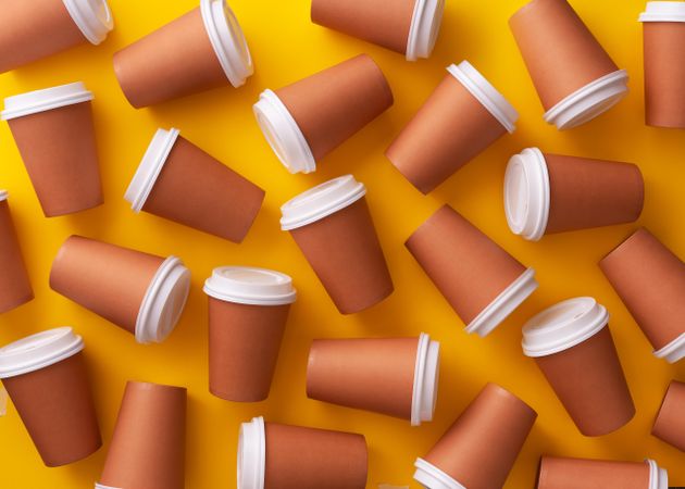 Scattered disposable coffee cups on yellow background