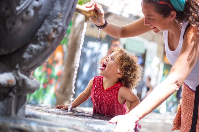 Woman pouring water from fountain for child on street