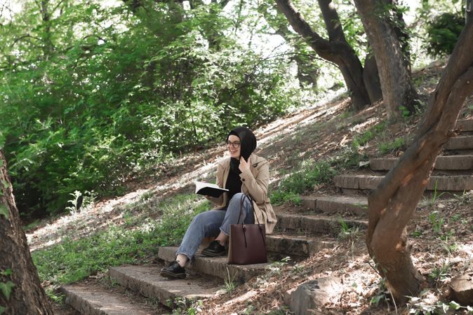 Smiling woman on outdoor staircase holding book