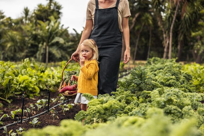 Adorable little girl standing in a vegetable garden with her mother behind her