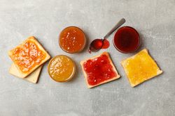 Bowls and toasts with jam on gray background, top view