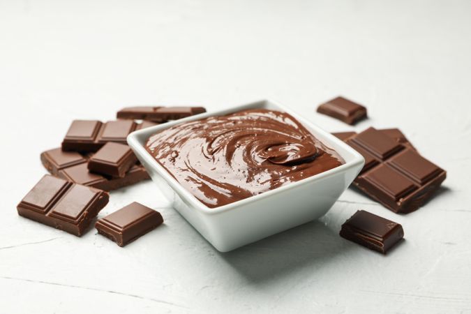 Bowl with chocolate and chocolate pieces on light background