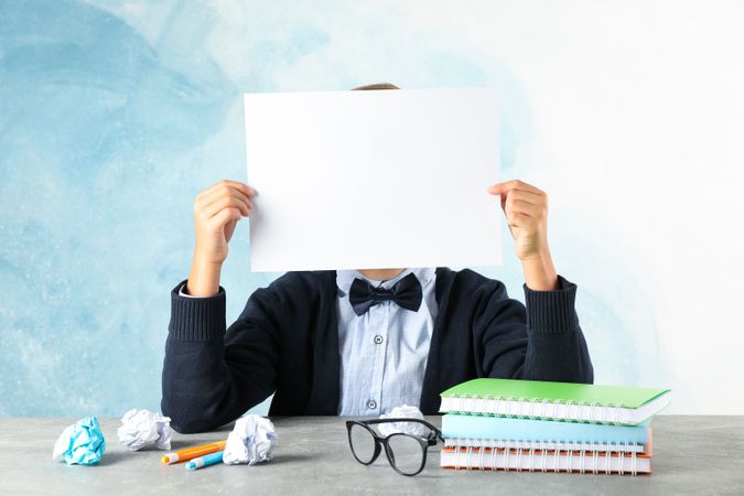Boy in school uniform hold empty paper against color background