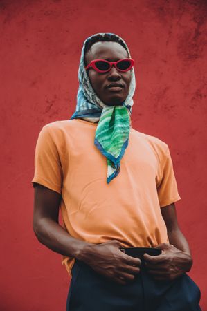 Man wearing headscarf and red framed sunglasses standing beside wall
