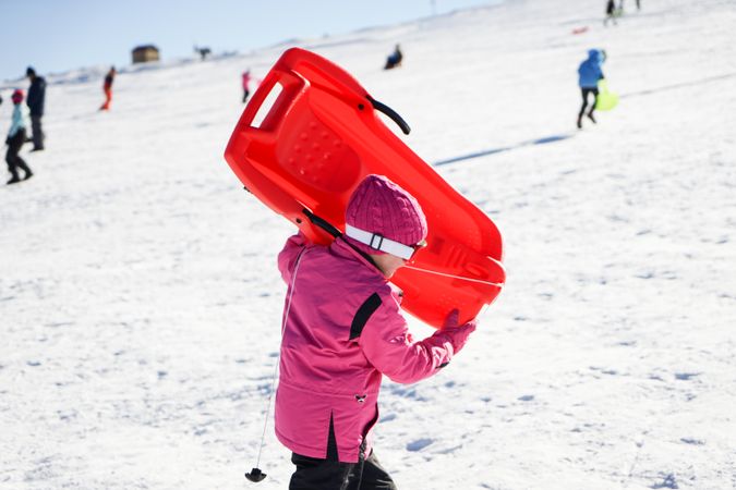 Child in pink snow suit holding sled at resort