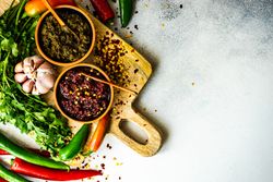 Looking down at pot of traditional Georgian sauce Adjika with garlic bulb & raw ingredient on wooden board with copy space