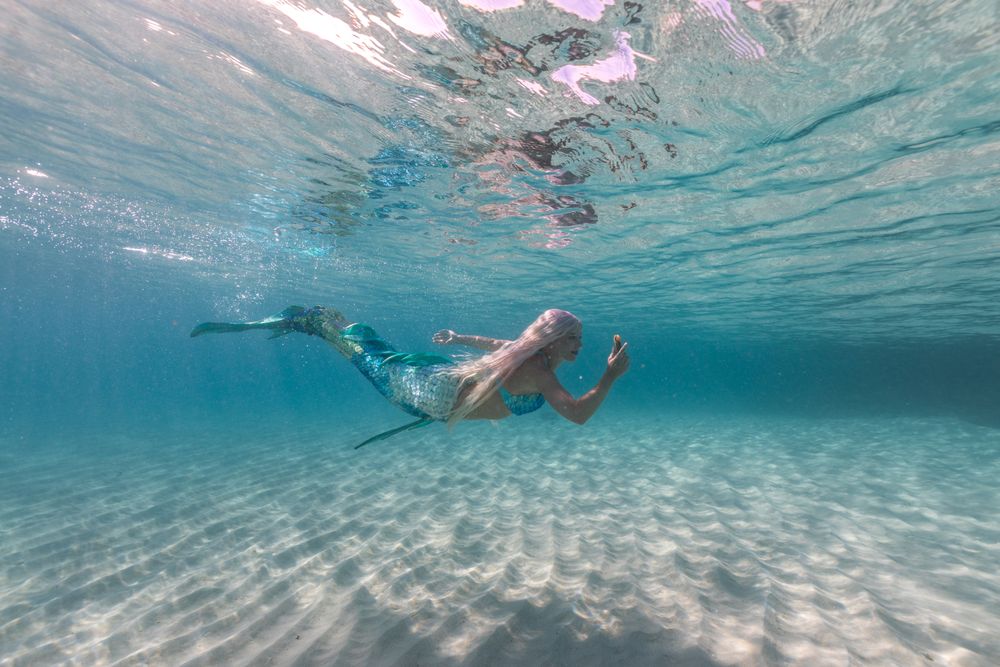 Blond fairytale female mermaid exploring underwater