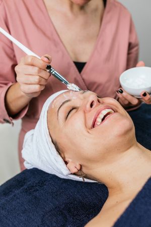 Anonymous professional beautician applying facial mask on face of client