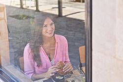 Cheerful woman eating delicious burger in cafe