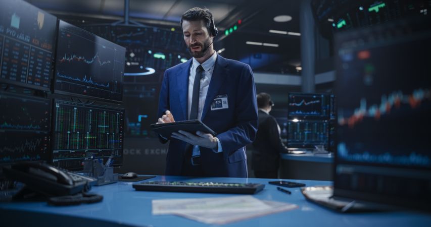 Portrait of a Young Handsome Stock Exchange Broker Working on a Tablet Computer, Researching Stocks Data, Analyzing Commodities and Exchange Market Charts.