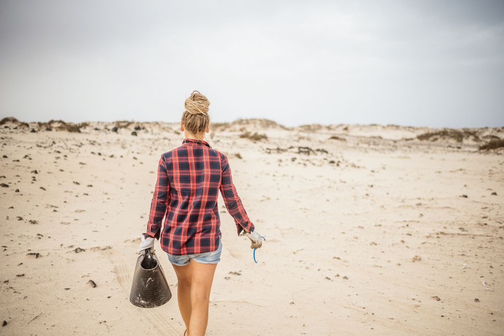 Content modern woman picking litter from sandy seashore