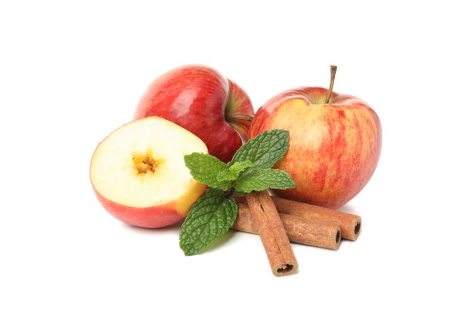 Side view of two apples, leaves, cinnamon sticks, and a pot of honey