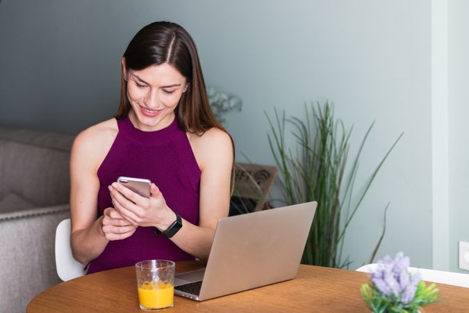 Smiling woman using smartphone and sitting at table with laptop
