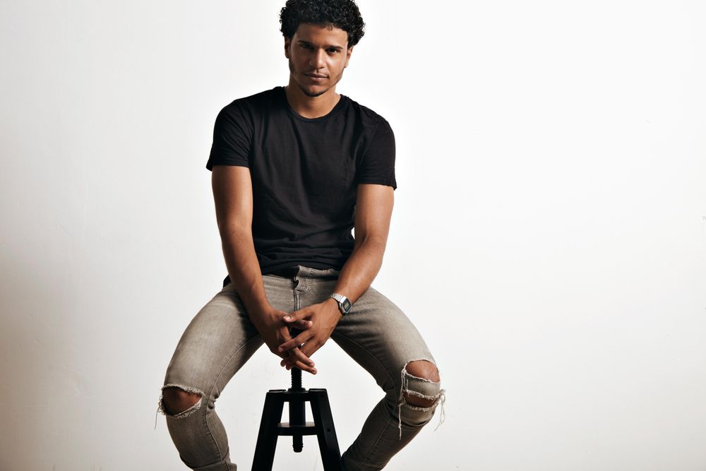 Serious man in dark clothes sitting on stool