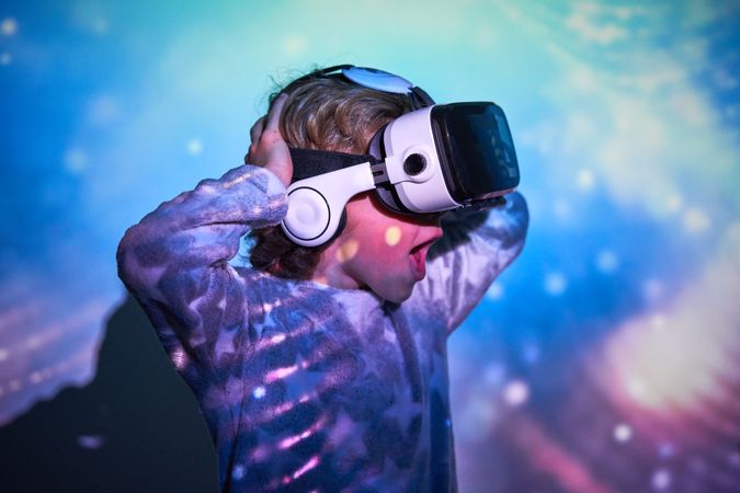 Astonished kid in VR headset shouting in illuminated room