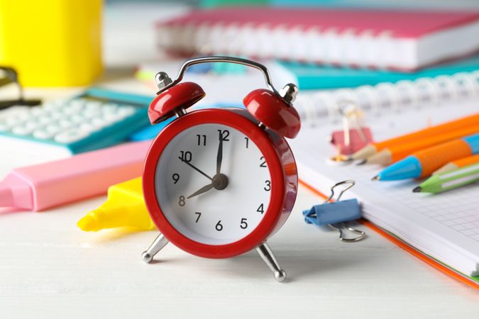 Red alarm clock on table surrounded by other school supplies