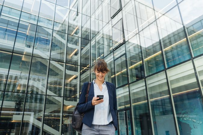 Smiling entrepreneur browsing smartphone outside office building