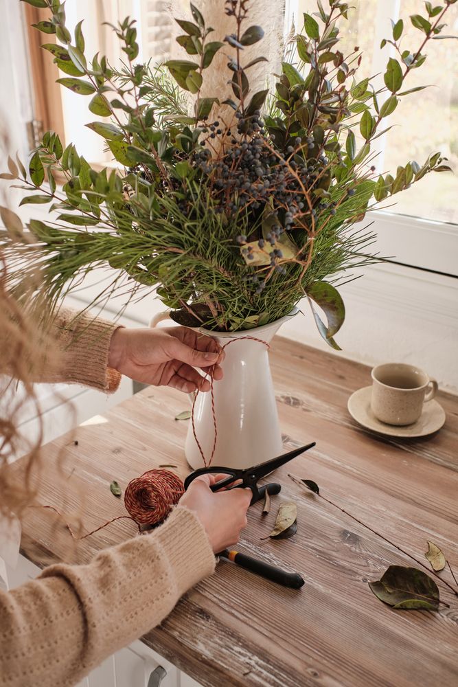 Crop florist preparing composition of green branches on table