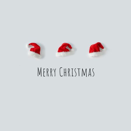 Santa hats in a row on light background above “Merry Christmas”