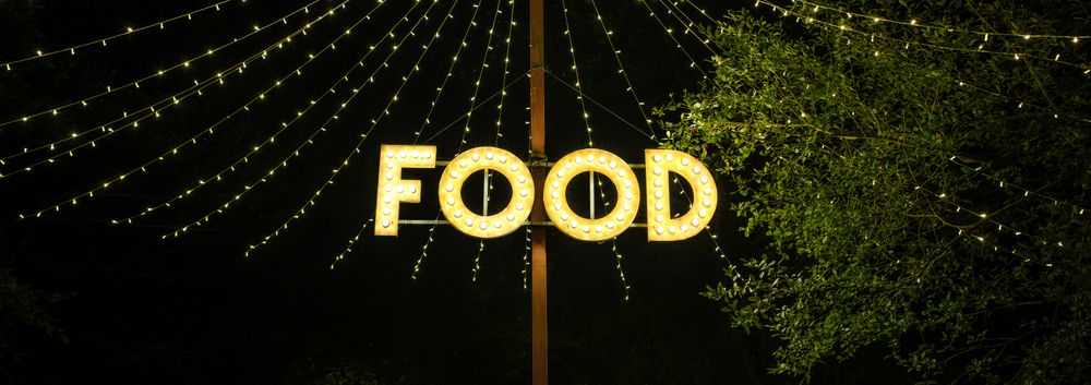 Signboard with word food made with light bulbs hung on wooden post under light garlands