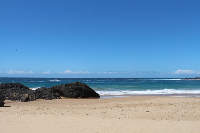 Beautiful sandy beach with rocks and clear blue ocean under sunny sky