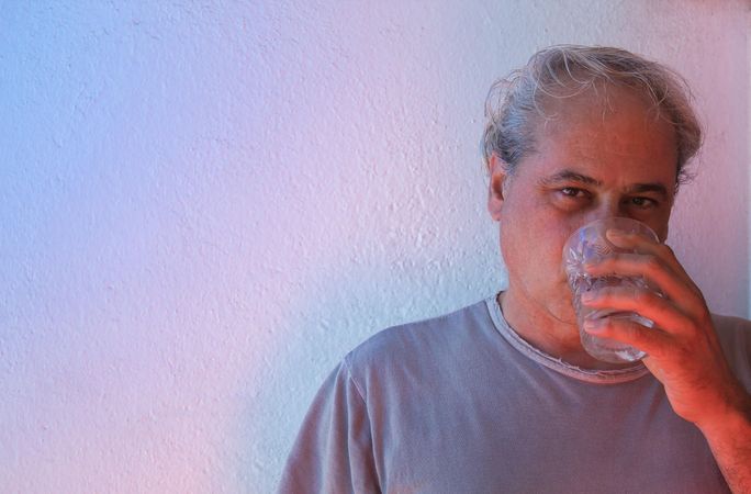 Portrait of middle aged man drinking water against light background in UV lit studio