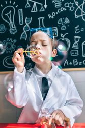 Kid blowing soap bubbles in front of drawings on chalkboard