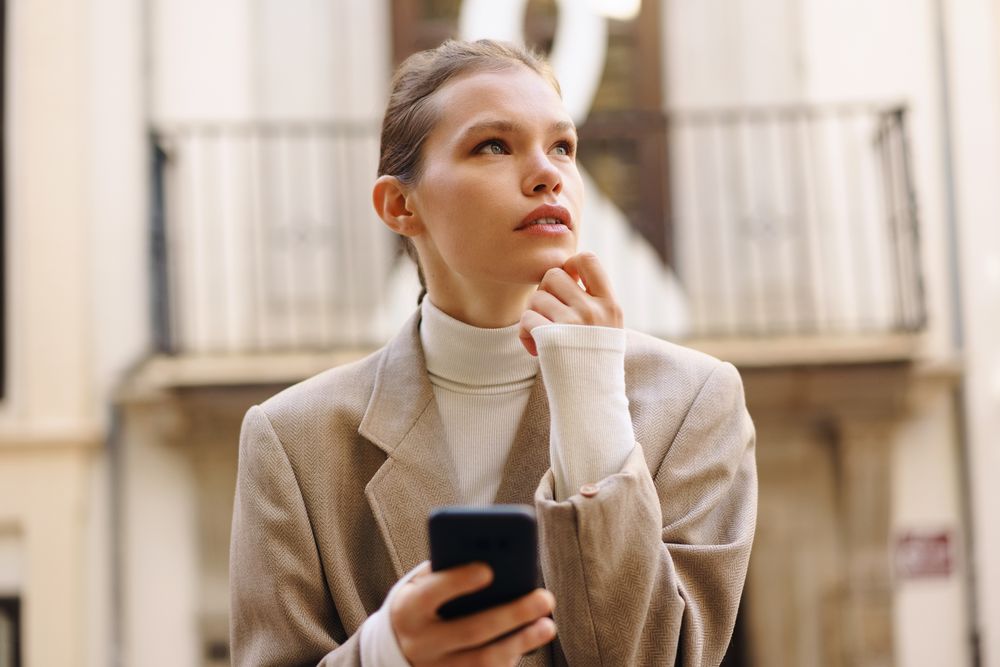A Young Woman Deep in Thought as She Engages with Her Smartphone in a Bustling Urban Setting