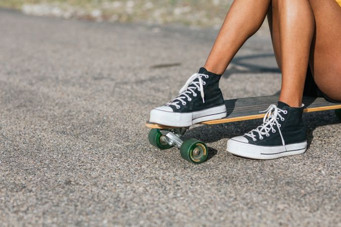Anonymous woman sitting on longboard on asphalt road