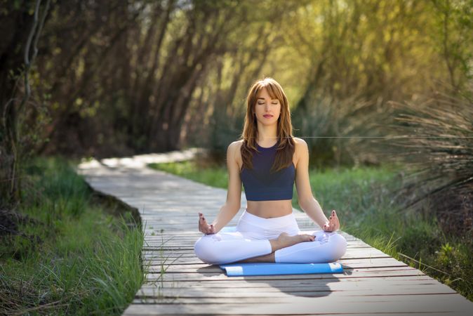Female wearing sport clothes meditating with eyes closed on yoga mat outside