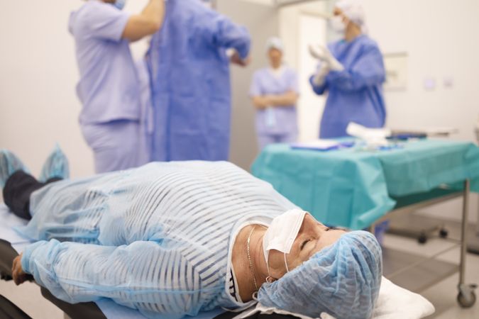 Mature woman in hair net and facemask lying down pre-surgery