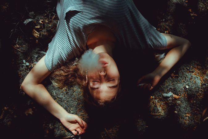 Woman with smoke from mouth lying on ground