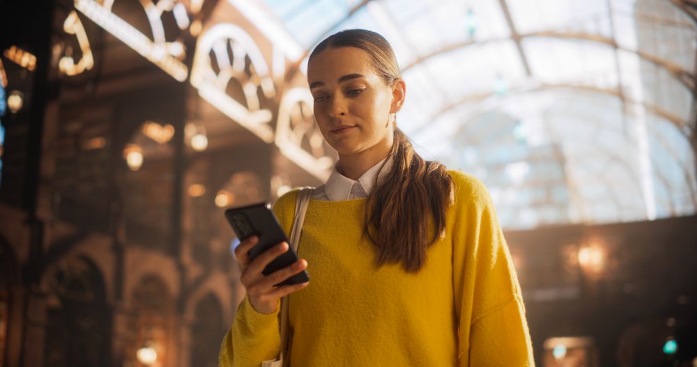 Young Female Using Smartphone in a Sunlit Historic Train Station.