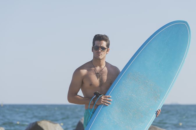 Male surfer holding surfboard standing in front of the coast