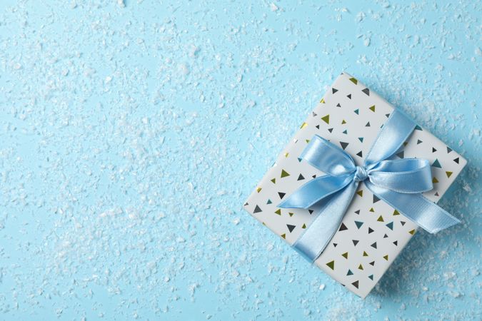 Snow and present with bow on blue background, space for text