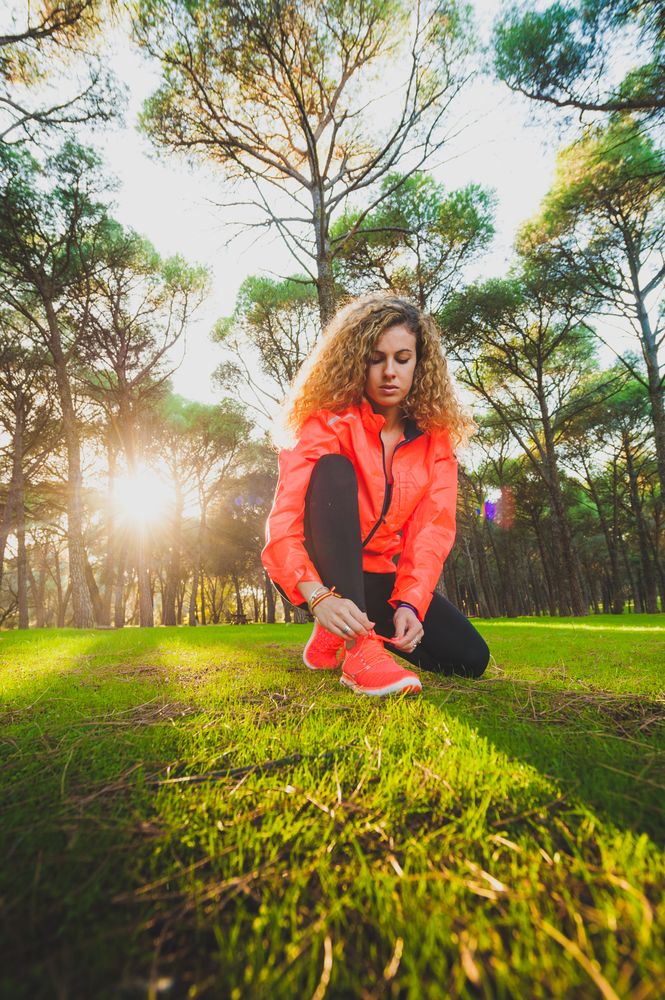 Woman tying shoelaces on meadow in sunlight