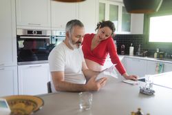 Silver baby shoes on counter as pregnant woman with man read book