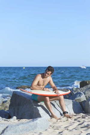 Male surfer relaxing near water with board on lap