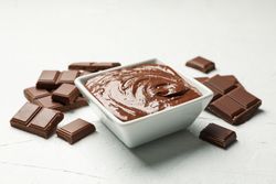 Bowl with chocolate and chocolate pieces on light background