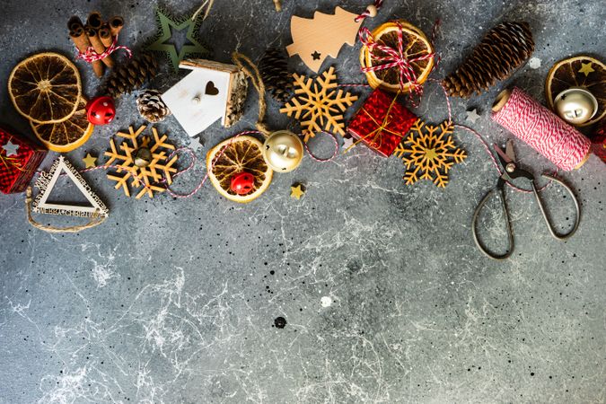 Wooden snowflakes and tree ornaments with dried orange slices, scissors and pine cones on marble table