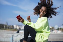 Carefree smiling female with curly hair in bright green shirt sitting listening to music outside