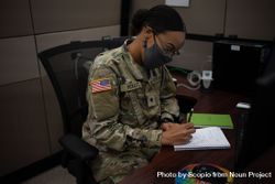 US female soldier with facemask sitting at her desk writing on notebook bxrLX5
