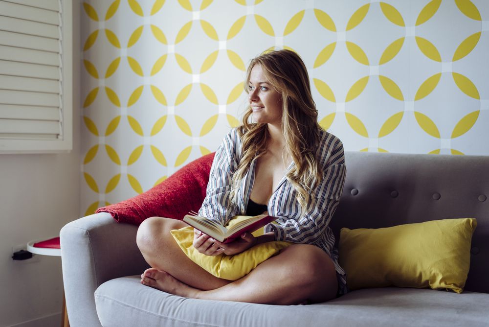 Young happy female reading book on sofa