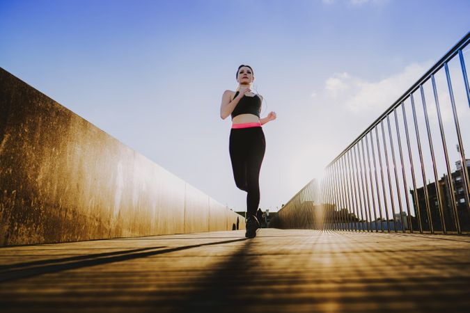 Woman running on walkway in sunny day with blue sky