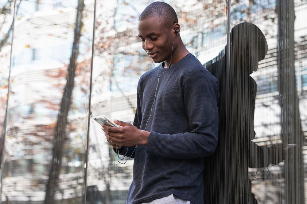 Black man listening to music in earphones on smartphone