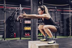 Athletic woman jumping on box to improve stamina in gym