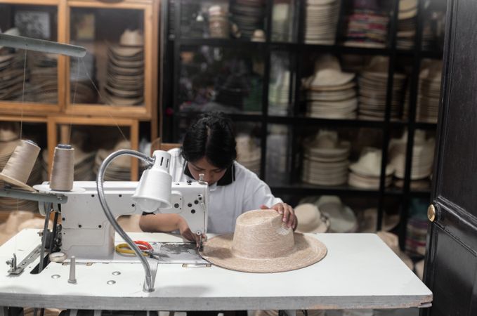 A young Hispanic woman is sewing a natural fiber hat