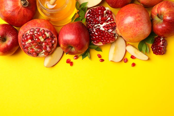 Top view of fresh apples, pomegranate and honey on yellow background with copy space